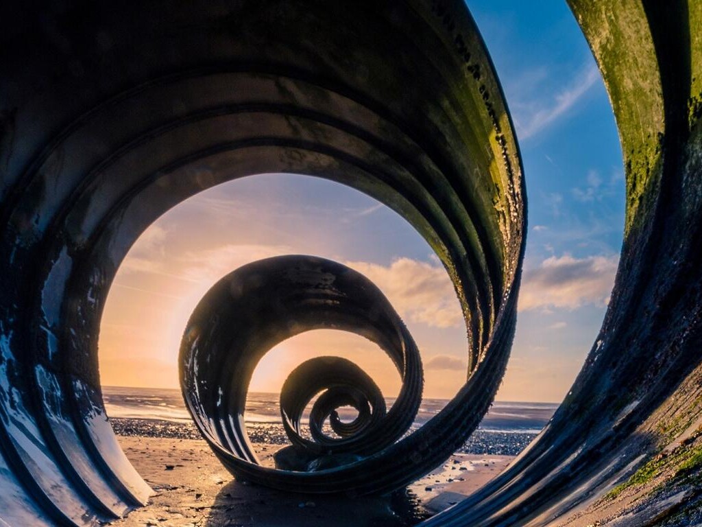 Eine Spirale aus Metall, durch die man den Sonnenuntergang am Strand sieht