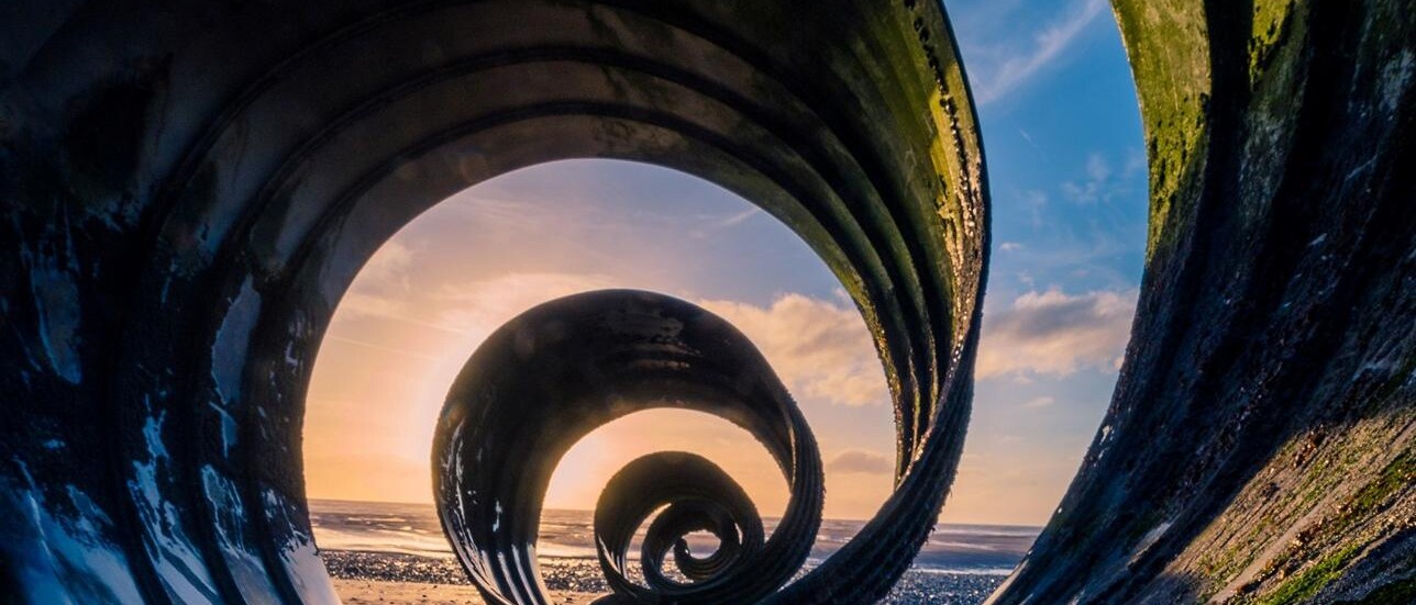 Eine Spirale aus Metall, durch die man den Sonnenuntergang am Strand sieht