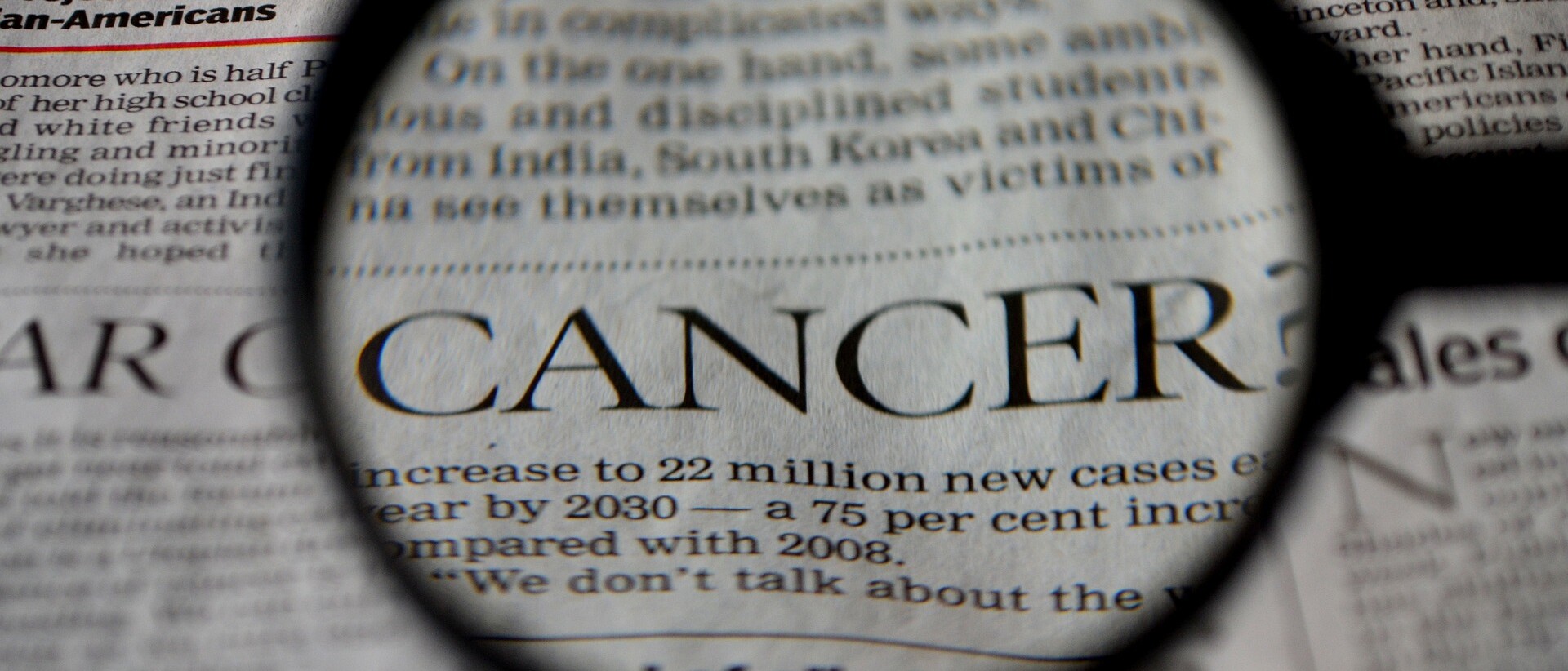 Das Bild zeigt einen englischen Zeitungsauschnitt bei dem das Wort Cancer mit einer Lupe vergrößert wird